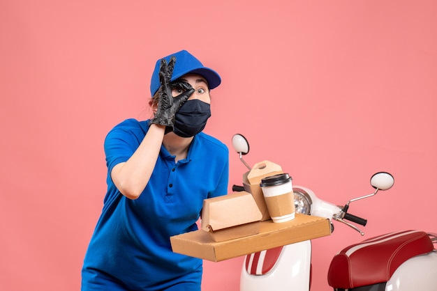 Front view female courier in mask with delivery coffee and food on pink 