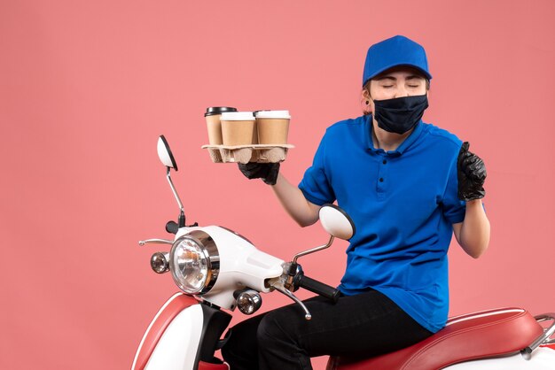 Front view female courier in mask with delivery coffee on pink 