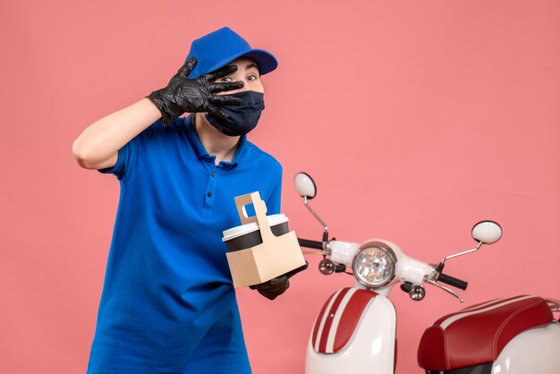 Front view female courier in mask with delivery coffee on pink 