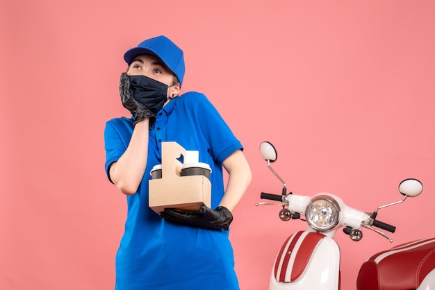 Front view female courier in mask with delivery coffee on pink 