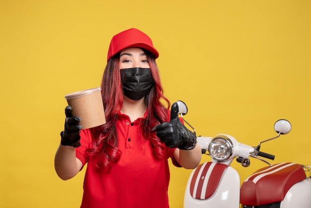 Front view of female courier in mask with delivery dessert on the yellow wall