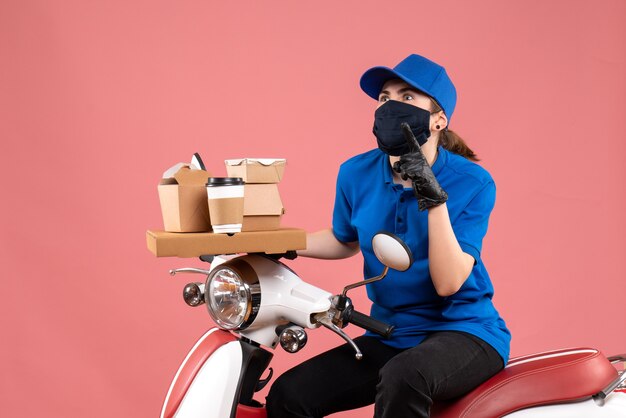 Front view female courier in mask with food delivery on pink 