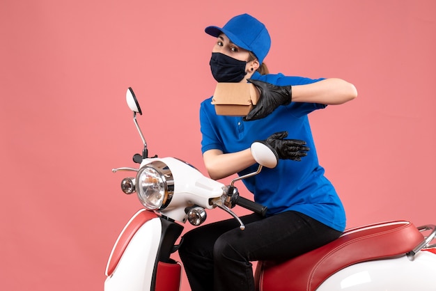 Free photo front view female courier in mask with little food package on pink