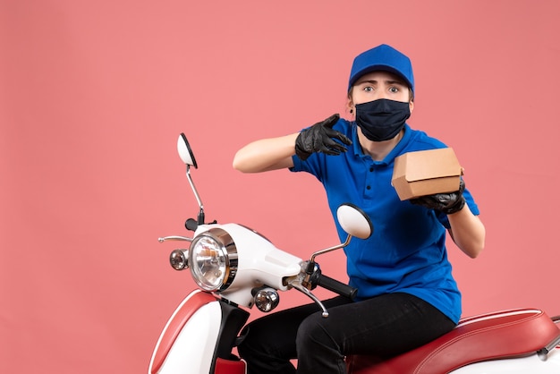 Front view female courier in mask with little food package on pink 