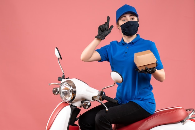 Front view female courier in mask with little food package on pink 