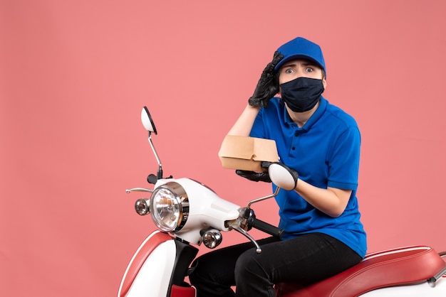 Front view female courier in mask with little food package on pink 