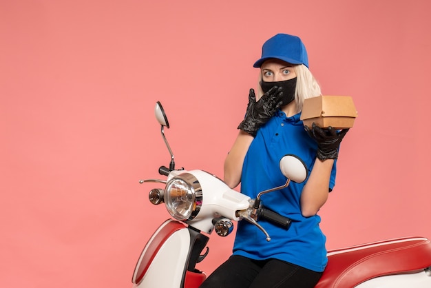 Front view female courier in mask with little food package on the pink 