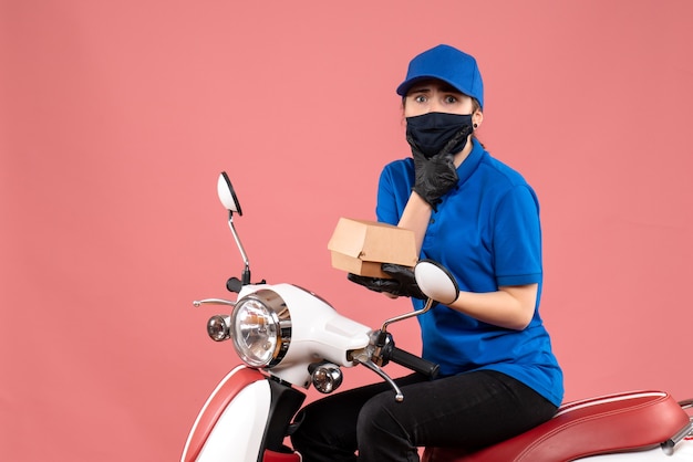 Front view female courier in mask with little food package on the pink 