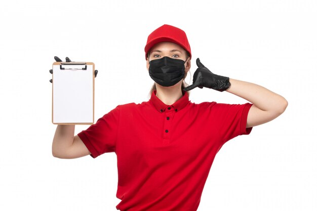 A front view female courier in red carp red shirt black gloves and black mask holding notepad and showing phone call sign on white