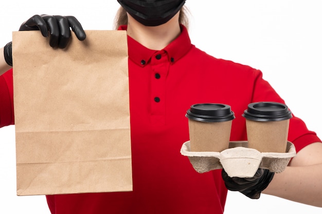 A front view female courier in red shirt andb lack glvoes holding coffee cups and package with food