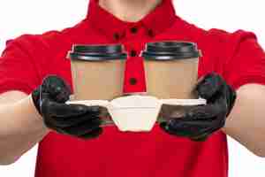 Foto gratuita un corriere femminile vista frontale in guanti neri camicia rossa in possesso di tazze di caffè