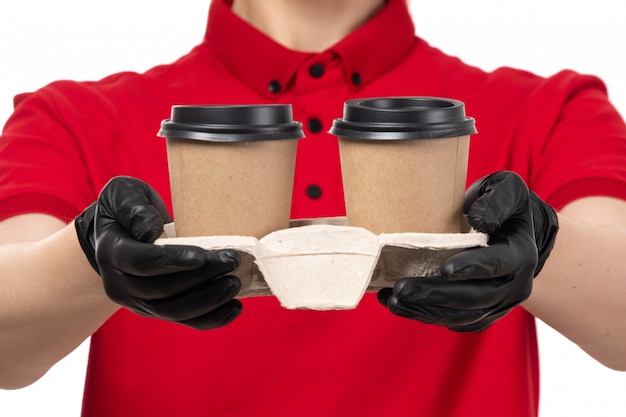 A front view female courier in red shirt black gloves holding coffee cups