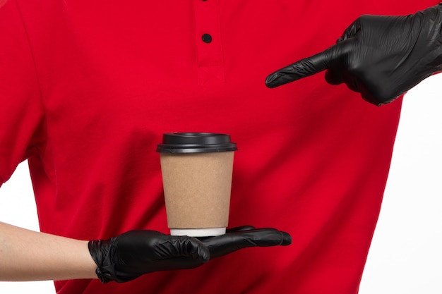 A front view female courier in red shirt black gloves holding coffee on white