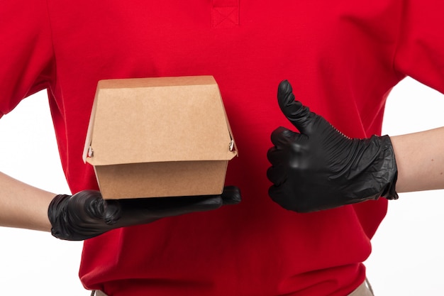 Вид спереди курьер женского пола в красной рубашке и черные перчатки, держа пакет с едой
