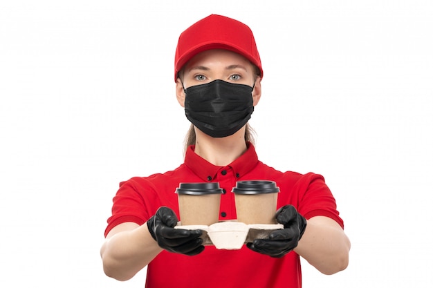 A front view female courier in red shirt red cap black gloves and black mask holding coffee cups