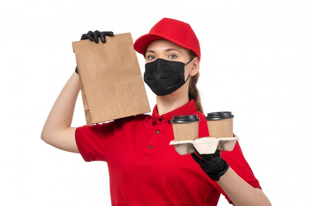 A front view female courier in red shirt red cap black gloves and black mask holding coffee and food packages