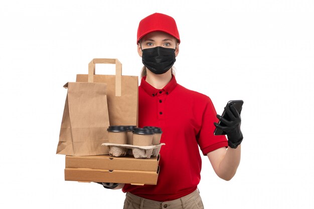 赤いシャツの赤い帽子の黒い手袋とコーヒーパッケージとスマートフォンを保持している黒いマスクの正面図女性宅配便