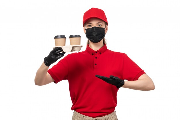 A front view female courier in red shirt red cap black gloves and black mask holding coffee