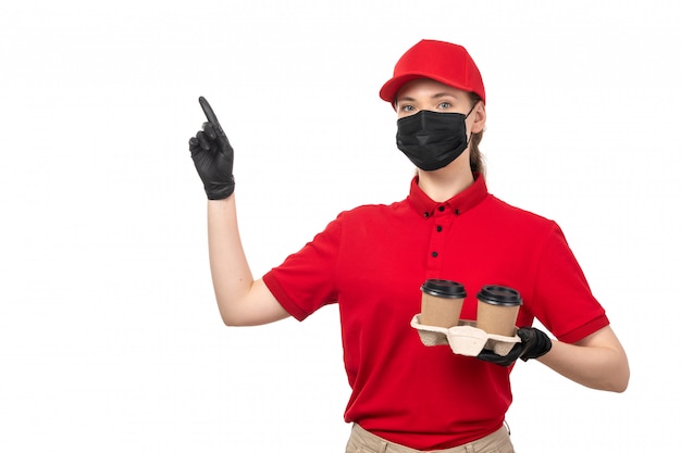 Free photo a front view female courier in red shirt red cap black gloves and black mask holding coffee