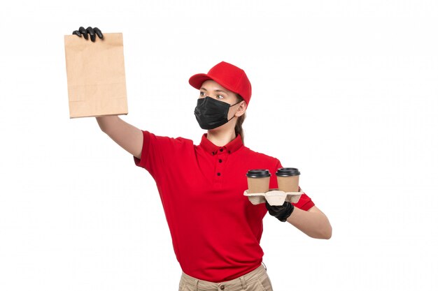 A front view female courier in red shirt red cap black gloves and black mask holding food package and coffee on white