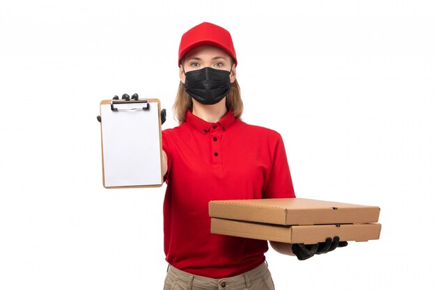 A front view female courier in red shirt red cap black gloves and black mask holding paper and pizza boxes on white job uniform