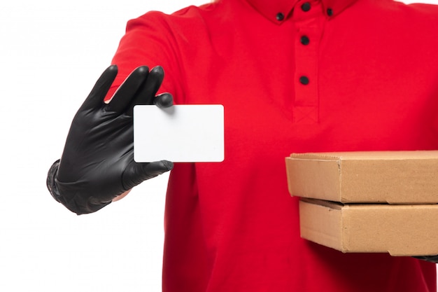 A front view female courier in red shirt red cap black gloves and black mask holding pizza boxes and white card on white