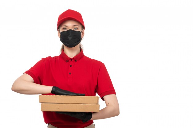 A front view female courier in red shirt red cap black gloves and black mask holding pizza boxes on white