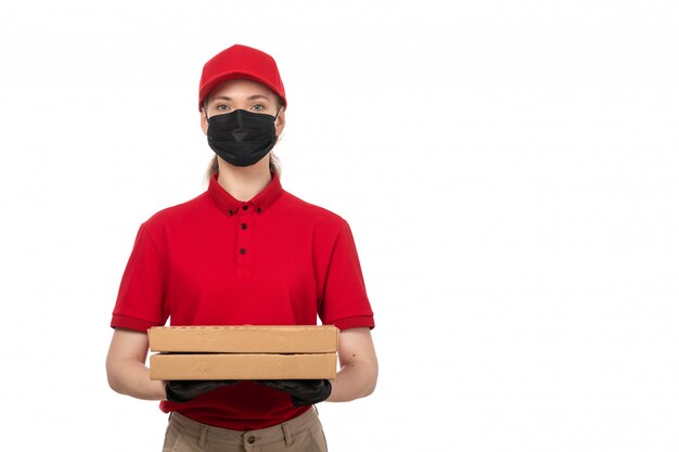 Вид спереди курьер женского пола в красной рубашке, красной шапочке, черных перчатках и черной маске с коробками для пиццы на белом