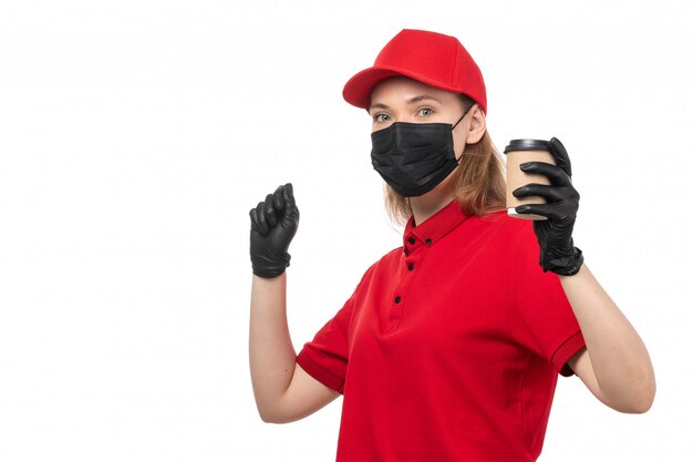 A front view female courier in red shirt red cap black gloves holding coffee on white