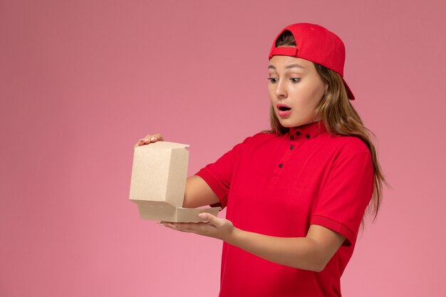 빨간 제복을 입은 여성 택배와 밝은 분홍색 벽에 배달 음식 패키지를 들고 케이프, 유니폼 배달 서비스 회사