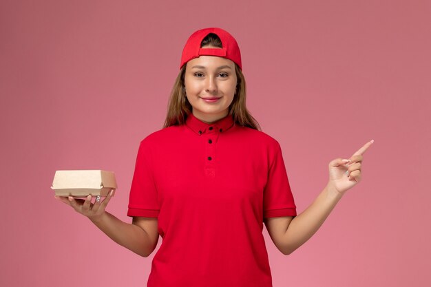 赤い制服を着た正面図の女性の宅配便とピンクの背景に配達食品パッケージを保持している岬制服配達サービス会社の労働者の仕事