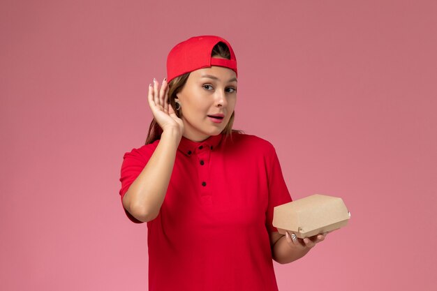 赤い制服を着た正面図の女性の宅配便とピンクの背景に配達食品パッケージを保持している岬制服配達サービス会社の労働者の仕事