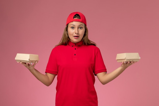 빨간색 유니폼과 밝은 분홍색 벽에 배달 음식 패키지를 들고 케이프, 유니폼 배달 서비스 회사 직업 소녀 전면보기 여성 택배