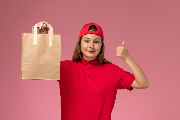 赤い制服とピンクの壁に配達紙パッケージを保持している岬の正面図の女性の宅配便、制服配達労働者サービス