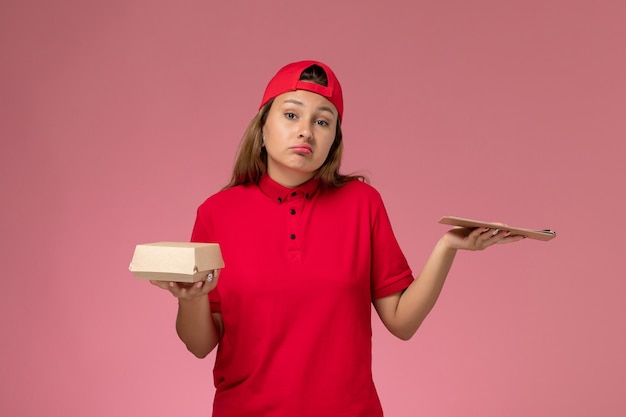 분홍색 벽에 작은 배달 음식 패키지와 메모장을 들고 빨간 유니폼과 케이프의 전면보기 여성 택배, 균일 한 배달 서비스 직업 회사