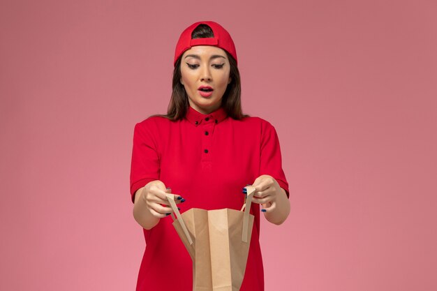 분홍색 벽, 작업자 유니폼 배달 직원에 그녀의 손에 배달 용지 패키지와 함께 빨간색 유니폼 케이프에서 전면보기 여성 택배