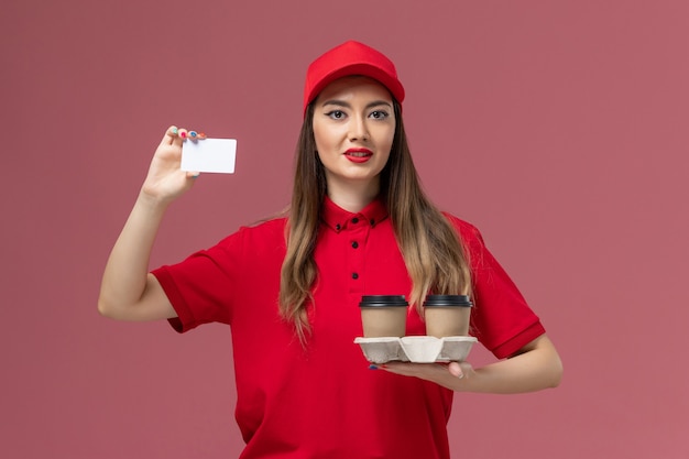 분홍색 배경 서비스 작업 배달 유니폼에 배달 커피 컵과 카드를 들고 빨간 유니폼에 전면보기 여성 택배