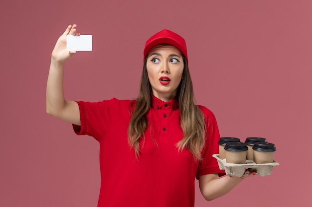 淡いピンクの背景に白いカードを保持している赤い制服の正面図女性宅配便サービス求人制服会社