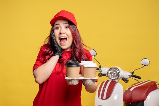Front view of female courier in red uniform with coffee on a yellow wall