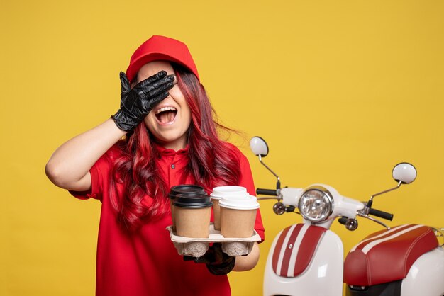 Front view of female courier in red uniform with coffee on the yellow wall