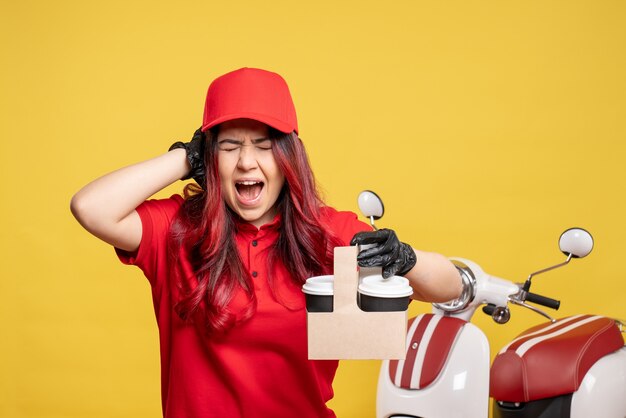 Front view of female courier in red uniform with coffee on the yellow wall