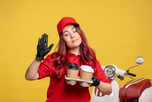 Front view of female courier in red uniform with coffee on yellow wall
