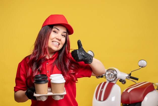 Front view of female courier in red uniform with coffee on yellow wall