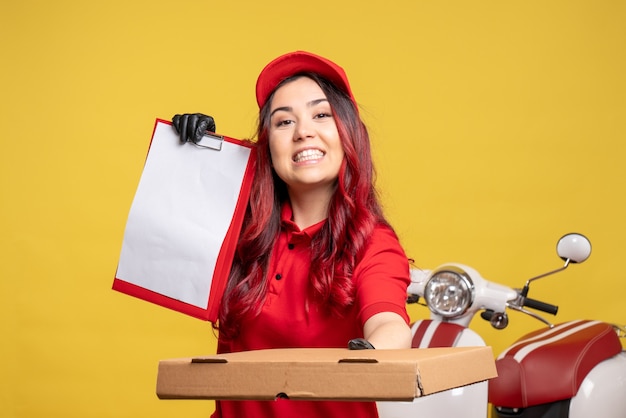 Foto gratuita vista frontale del corriere femminile in uniforme rossa con nota di file e scatola di cibo sulla parete gialla