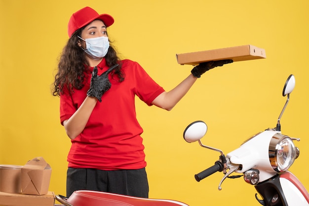 Front view female courier in red uniform with pizza box on yellow background service covid- pandemic virus job delivery