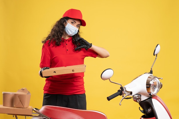 Free photo front view female courier in red uniform with pizza box on yellow background service worker covid- pandemic virus job