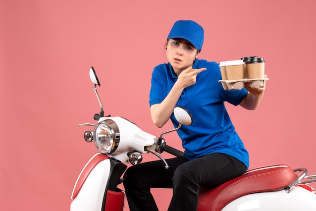 Front view female courier sitting on bike with coffee cups on pink color uniform job worker food service