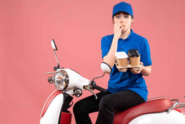 Front view female courier sitting on bike with coffee cups on pink color uniform service delivery job food