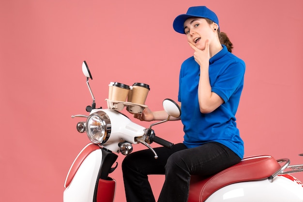 Front view female courier sitting on bike with coffee cups on pink job color uniform delivery worker food