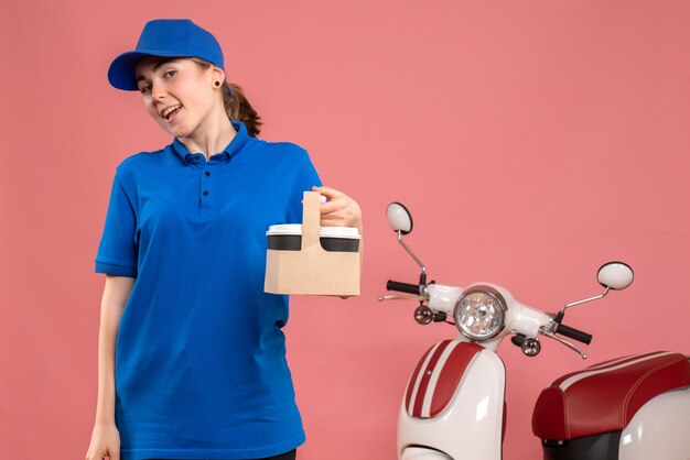 Front view female courier with delivery coffee on pink floor work delivery service worker woman bike uniform job